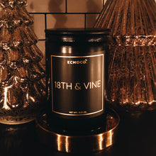 Load image into Gallery viewer, KCMOCO. Candles 18th &amp; Vine Candle in Classic Collection Jar: Black glass jar with gold foil label reading &quot;KCMOCO. 18th &amp; Vine&quot;, with black bamboo lid, environmental photo against backdrop of gold Christmas trees.
