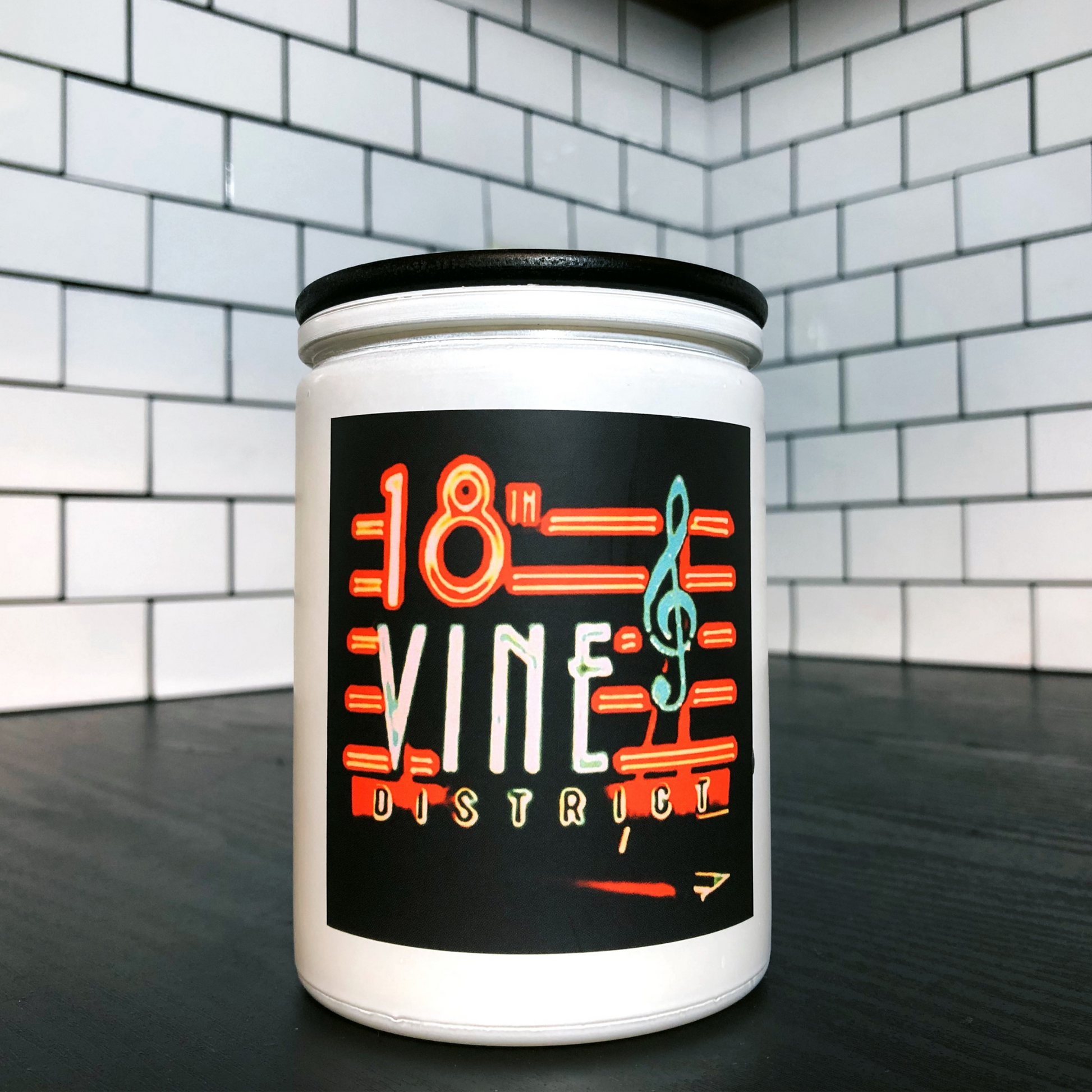 KCMOCO. 18th & Vine Candle in KC Collection Jar: White glass jar with photo label with photo of 18th & Vine neon sign, with black bamboo lid on kitchen cabinet..