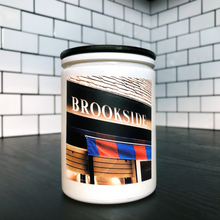Load image into Gallery viewer, KCMOCO. Brookside Blvd. Candle in KC Collection Jar: White glass jar with photo label depicting Brookside Shops awning, with black bamboo lid, on kitchen cabinet.
