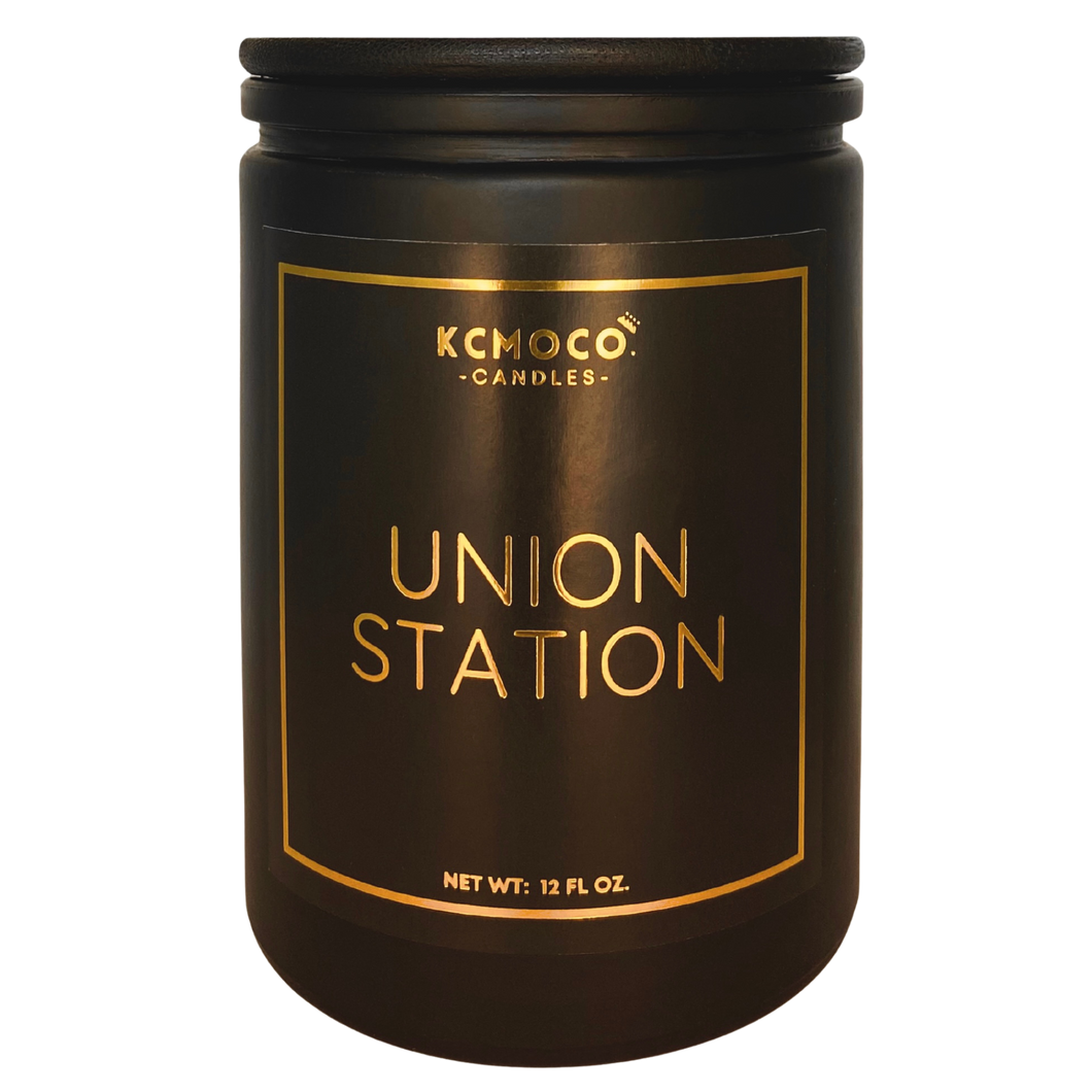 Black candle jar with gold foil label reading: KCMOCO. Candles UNION STATION Net Wt: 12 Fl Oz