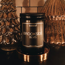 Load image into Gallery viewer,  KCMOCO. Candles Brookside Blvd. Candle in Classic Collection Jar: Black glass jar with gold foil label reading &quot;KCMOCO. Brookside Blvd.&quot;, with black bamboo lid, environmental photo against backdrop of gold Christmas trees.
